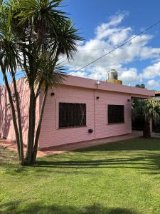 a pink building with a palm tree in a yard at Cabaña El Solcito, con parque y pileta compartida in Chascomús