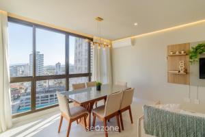 a dining room with a table and chairs and a large window at Apartamentos Bem Equipados a 100 m da Praia - EVR in Perequê