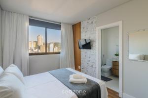 a white bedroom with a view of a city at Apartamentos Bem Equipados a 100 m da Praia - EVR in Perequê +31 photos