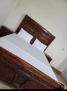una cama de madera con sábanas y almohadas blancas en Royal Inn Guest House, en Harīpur