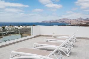 Una fila de sillas blancas en un balcón con vista al océano. en Los Ajaches - Caracolas, en Mácher