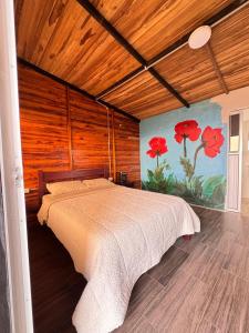 ein Schlafzimmer mit einem Bett und einem Gemälde von roten Blumen in der Unterkunft Costa Azul Refugio Frailejon in Tibasosa