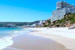 a beach with buildings on a hill next to the ocean at Estrela do Mar - Ocean View Apartment - Sesimbra - Falésia in Sesimbra