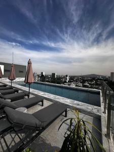 a pool with lounge chairs and umbrellas on a roof at Loft Americana Chapultepec Alberca Wifi AC in Guadalajara