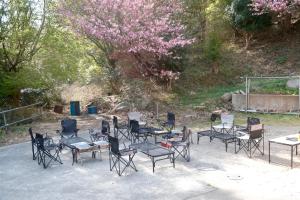 a group of chairs and tables and a tree with pink flowers at ARUYOguesthouse 一棟貸切 大人数でbbqと焚き火を楽しむ in Haibara