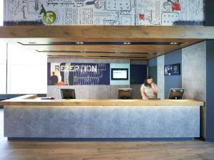 a woman standing at a reception counter in a lobby at ibis budget Basel City in Basel