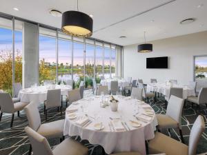 a dining room with white tables and chairs and windows at Mercure Melbourne Caroline Springs in Caroline Springs