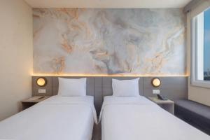 two beds in a room with a marble wall at Zest Jemursari by Swiss-Belhotel International in Surabaya +39 photos