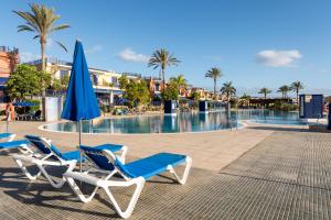 two lounge chairs and an umbrella next to a swimming pool at Oasis Beach Home Meloneras with jacuzzi in Maspalomas