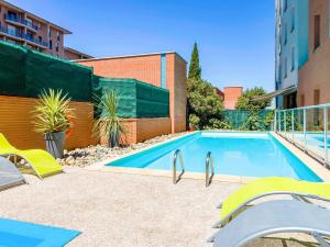 a swimming pool with yellow chairs next to a building at Aparthotel Adagio Access Toulouse Jolimont in Toulouse