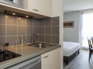 a kitchen with a sink and a bed in a room at Aparthotel Adagio Access Avignon in Avignon