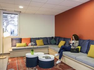 eine Frau, die auf einer Couch in einem Zimmer sitzt in der Unterkunft Aparthotel Adagio Access Paris Asnières in Asnières-sur-Seine