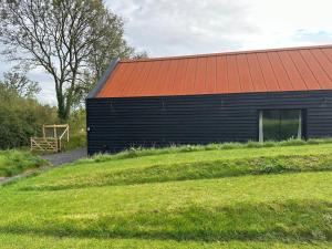 a black building with an orange roof next to a field at Contemporary modern barn in Folkestone