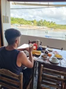 a young man sitting at a table with a meal at Pousada Nativa - Vista ao mar in Ilha de Boipeba