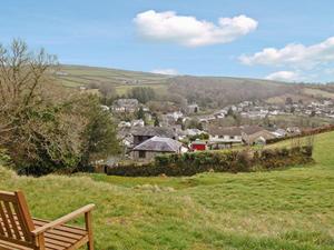 a wooden bench sitting in a field with a town at Tripp Cottage in Saint Neot