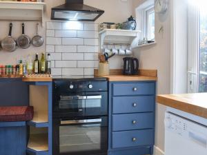 a kitchen with a black stove and blue cabinets at Vine Cottages in Crich