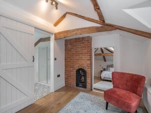 een woonkamer met een bakstenen open haard en een rode stoel bij Clematis Cottage in Thorpe Market