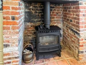 een kachel in een bakstenen open haard met een emmer bij Clematis Cottage in Thorpe Market