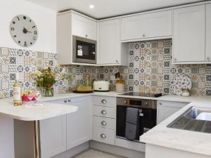 a kitchen with white cabinets and a clock on the wall at Pickled Onion Cottage in Taunton
