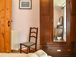 a bedroom with a wooden cabinet and a chair at Church House Cottage in Ulpha +15 photos