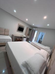 a white bedroom with two beds and a television at Pousada Bela By Bia - Comfort in Penha