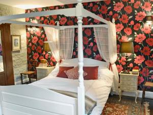 ein Schlafzimmer mit einem weißen Himmelbett mit Blumentapete in der Unterkunft Ragwood Cottage in Weare