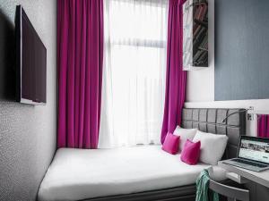 a bedroom with a bed with pink curtains and a laptop at ibis Styles Amsterdam Amstel in Amsterdam