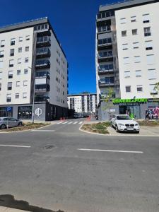 a street with two tall buildings and a white car at PARK NOVI Apartmani in Novi Sad