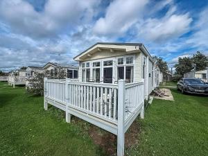 a white house with a porch on a lawn at 6 Berth Caravan For Hire At California Cliffs In Scratby By The Beach Ref 50050L in Great Yarmouth