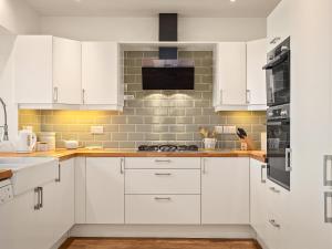 una cucina con mobili bianchi e un forno a piano cottura di Carew Cottage a Manorbier