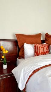 a bed with orange and white sheets and a vase with flowers at Velvet Oasis Mbabane in Mbabane
