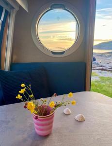 a vase of flowers sitting on a table with a window at Enkel, romslig og kul campingvogn in Moskenes
