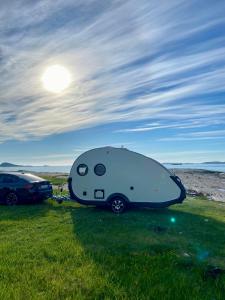 a white caravan parked in a field with a car at Enkel, romslig og kul campingvogn in Moskenes