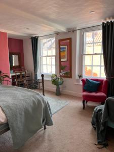 a bedroom with a bed and a red chair and windows at Flemish House in Beccles
