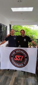 two men standing behind a table with a sign on it at Be Diving House in Cozumel
