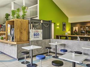 a restaurant with tables and stools in front of a counter at Ibis Budget Versailles Coignieres in Coignières