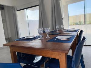 a wooden table with wine glasses and blue chairs at Galinhos Kite House - Casa à beira-mar para Kite, família e relaxamento in Galinhos