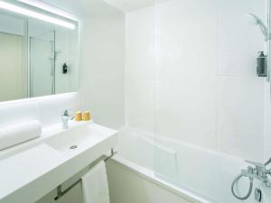 a white bathroom with a white tub and a sink at ibis budget Nantes Sainte Luce - Hôtel Rénové in Sainte-Luce-sur-Loire +56 photos
