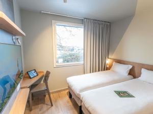 a hotel room with two beds and a desk and a window at Hotel Ibis Budget Rennes Cesson in Cesson-Sévigné