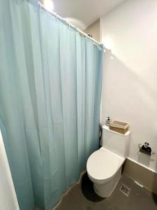 a bathroom with a toilet and a blue shower curtain at The Coastal Cove - One Bedroom in Iloilo City