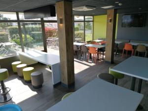 a restaurant with white tables and chairs and windows at ibis budget Bergerac in Bergerac