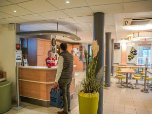 a man standing at a counter in a store with a baby at Ibis Budget Bayeux in Bayeux