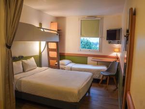 a hotel room with two beds and a desk at Ibis Budget Bayeux in Bayeux