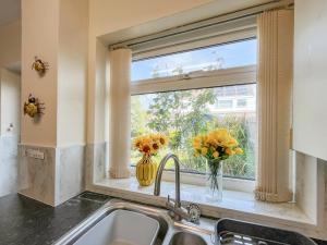 a kitchen window with flowers in a vase on a sink at Little Orme Cottage in Penrhyn Bay