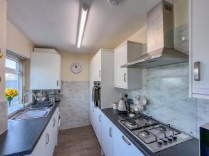 a kitchen with white cabinets and a stove and a sink at Little Orme Cottage in Penrhyn Bay