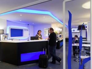 a man and a woman standing at a counter in an office at ibis budget Albertville in Gilly-sur-Isère