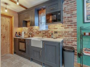 a kitchen with gray cabinets and a brick wall at The School House Cottage in Bradwell on Sea