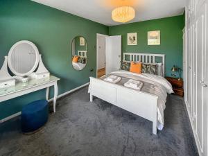 a bedroom with a white bed and green walls at Duckling Cottage in Canterbury