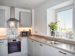 une cuisine avec des armoires blanches, un évier et un micro-ondes dans l'établissement Tosside Fold Cottage, à Tosside