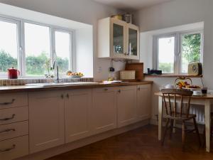 a kitchen with white cabinets and a sink and windows at Tre Anna Lodge in Dwyran